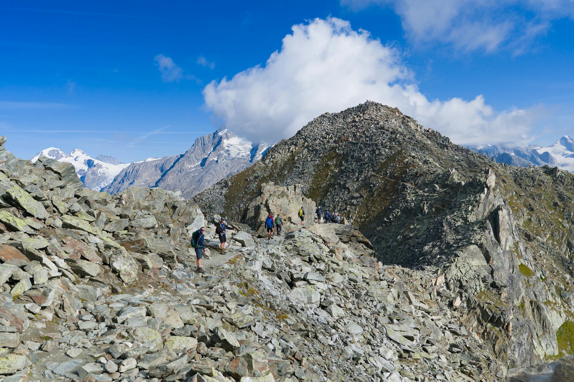 Turyści na kamienistym szlaku w Alpach Szwajcarskich przy błękitnym niebie