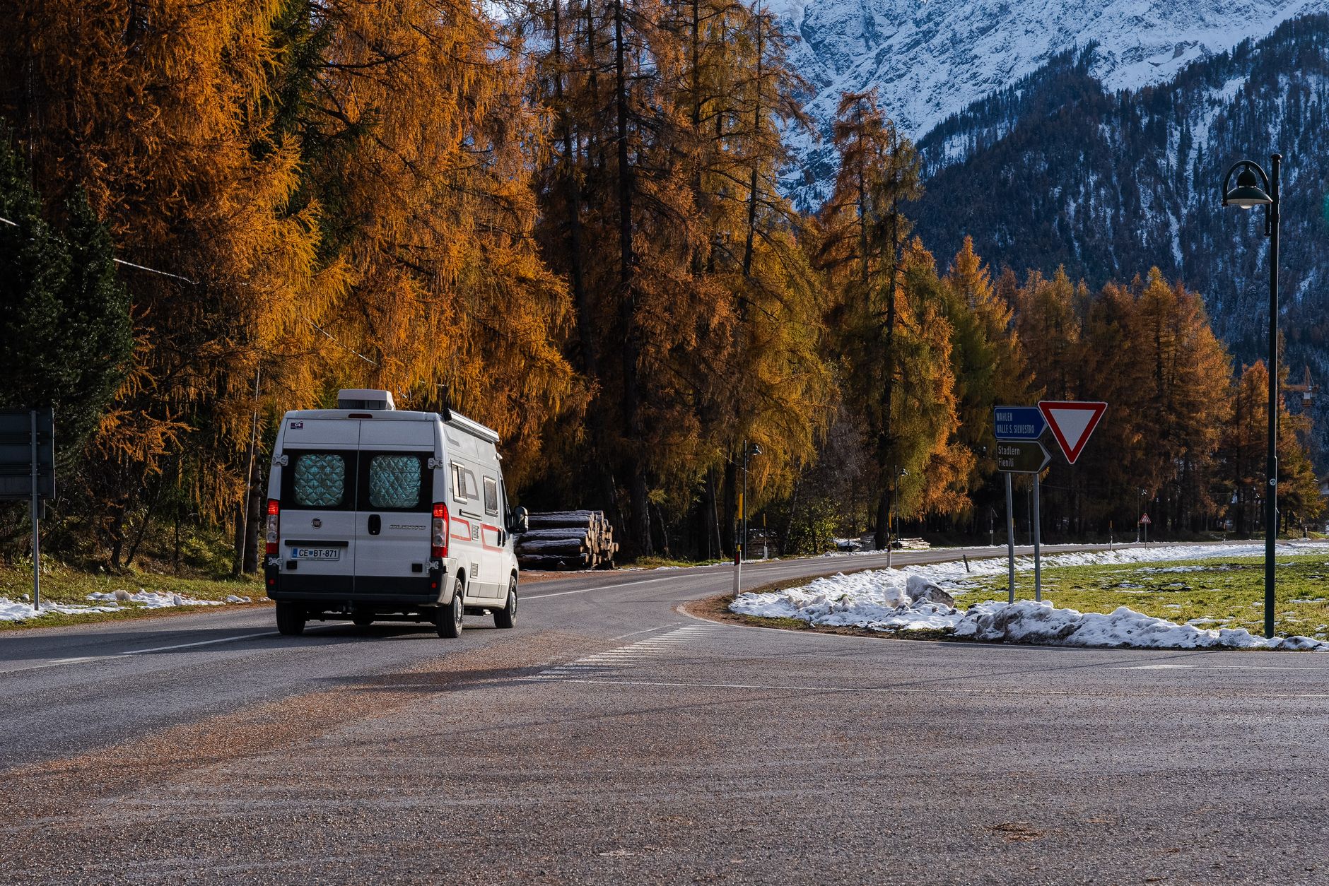 Kamper jedzie górską drogą w Alpach, jesienne lasy i śnieg