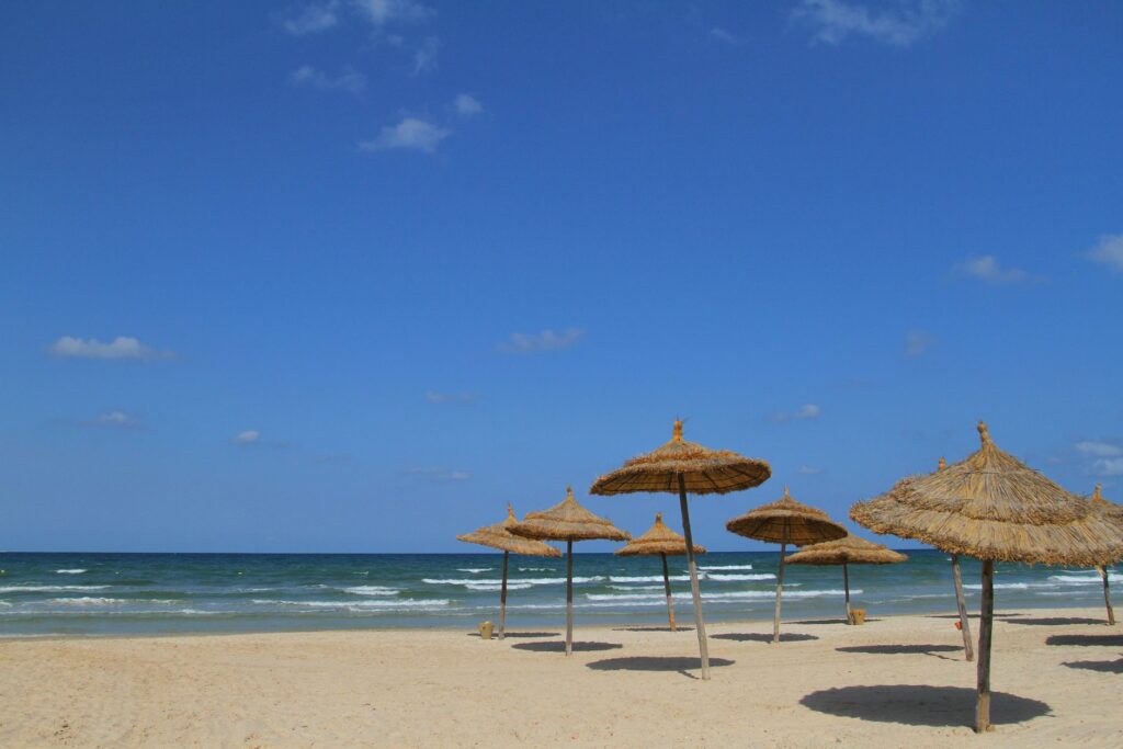 Słoneczna plaża w Tunezji ze słomianymi parasolami i błękitnym niebem